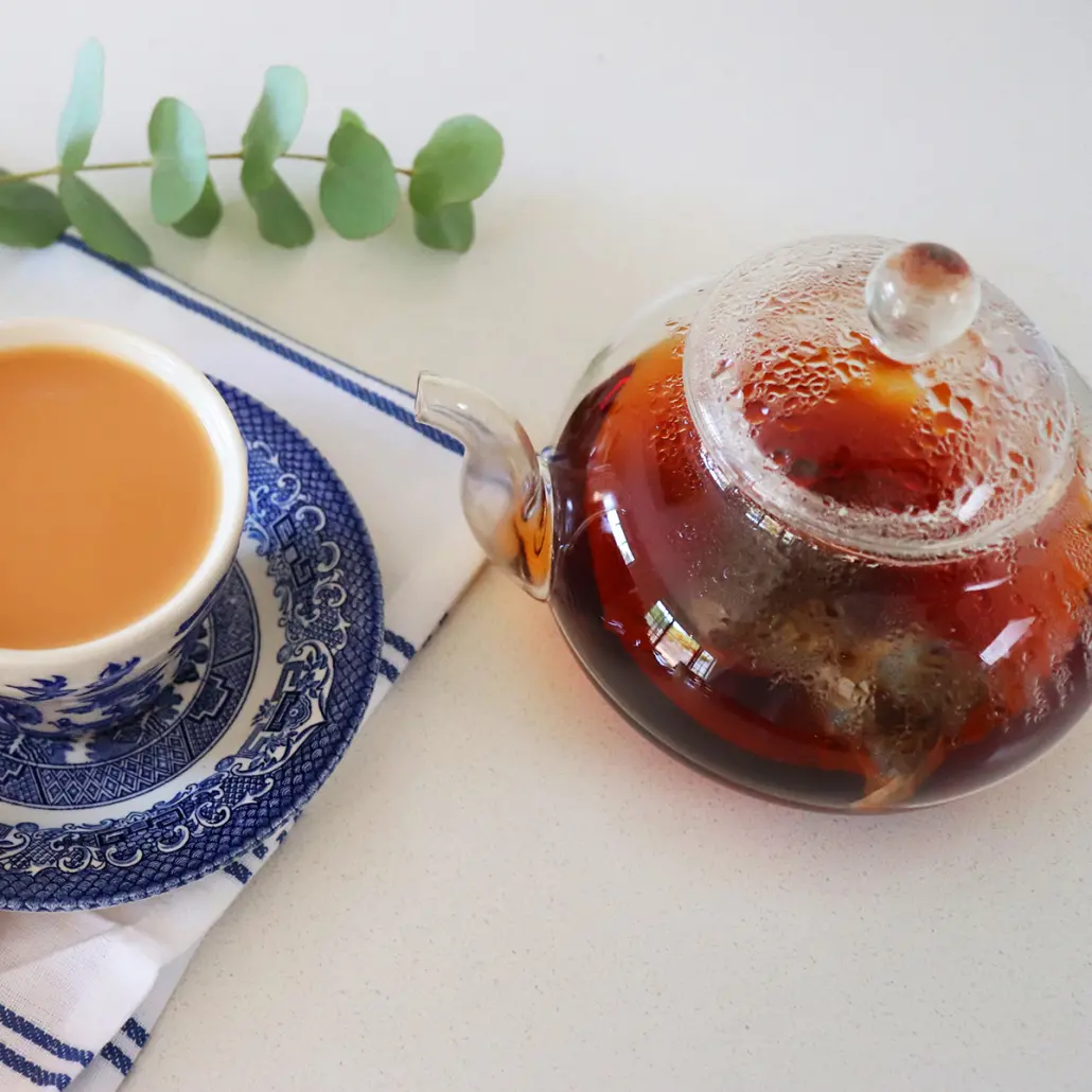 Fresh Carmién Tea in a glass teapot with brewed herbal tea and a traditional ceramic cup of tea on a blue patterned saucer, perfect for a healthy, antioxidant-rich beverage.