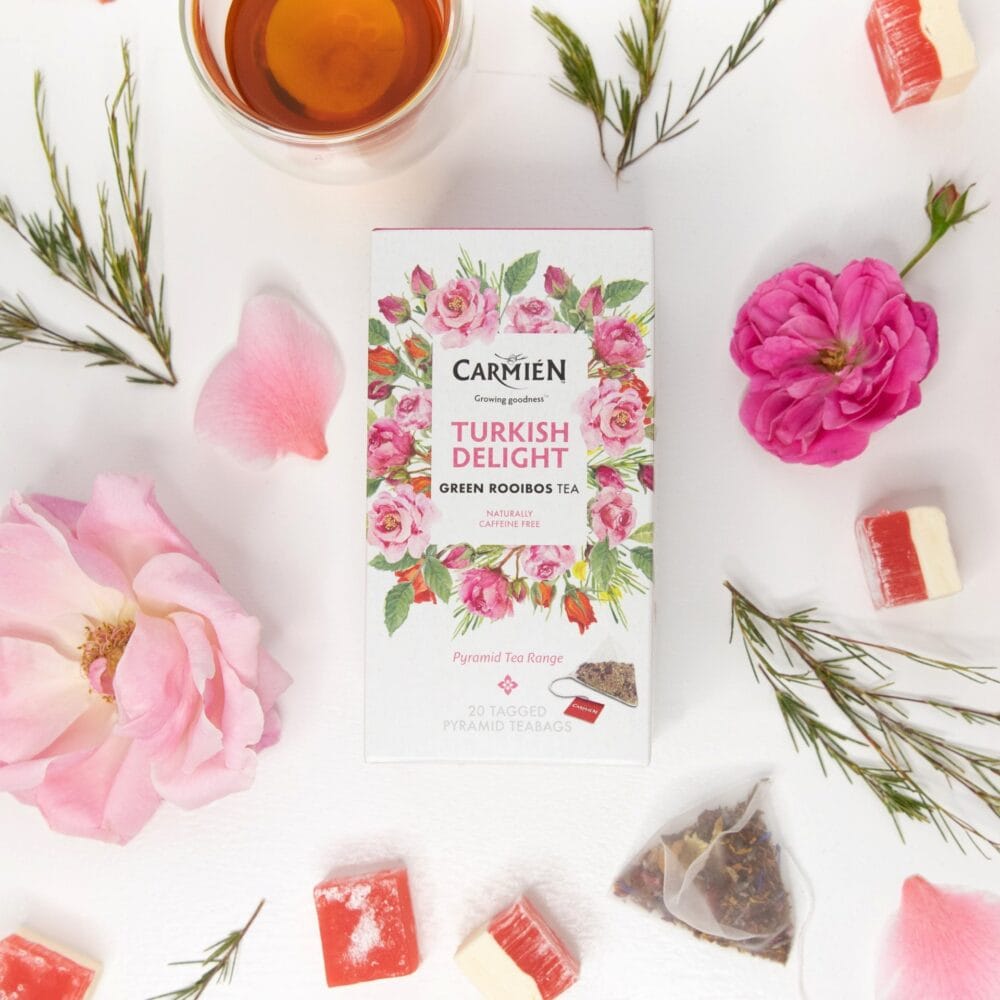 Carmién Turkish Delight Rooibos tea box with pyramid teabags surrounded by flowers and tea treats, highlighting the premium rooibos tea blend for e-commerce.