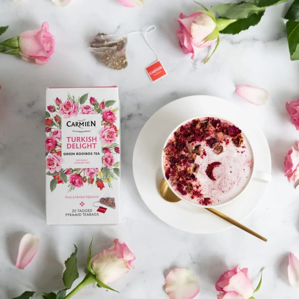 Carmién Turkish Delight Rooibos Tea box with a cup of brewed tea, surrounded by pink roses and tea ingredients, highlighting the premium rooibos tea blend.