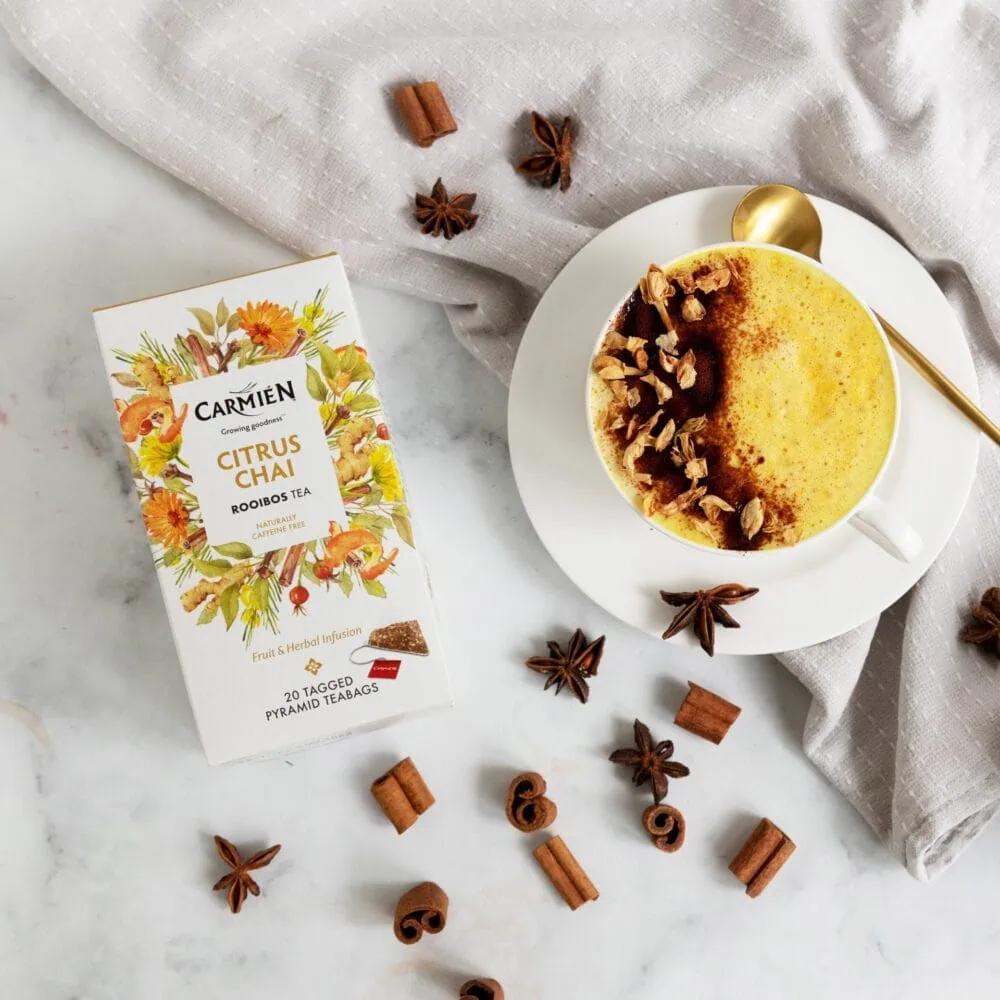 Carmién Citrus Chai Rooibos Tea in a cup with spices and tea box on a white surface.