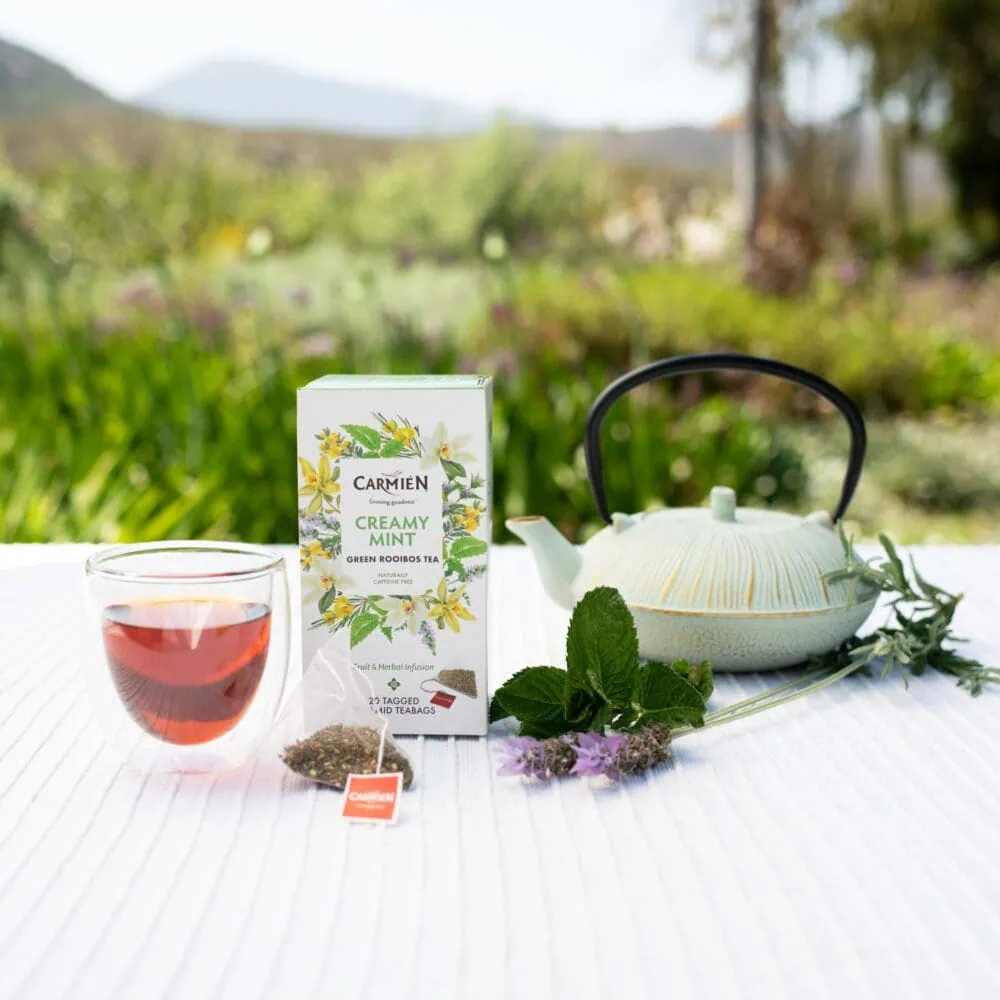 Carmién Tea Creamy Mint rooibos tea with fresh mint leaves and teapot on outdoor table, promoting herbal tea blends for health and relaxation.