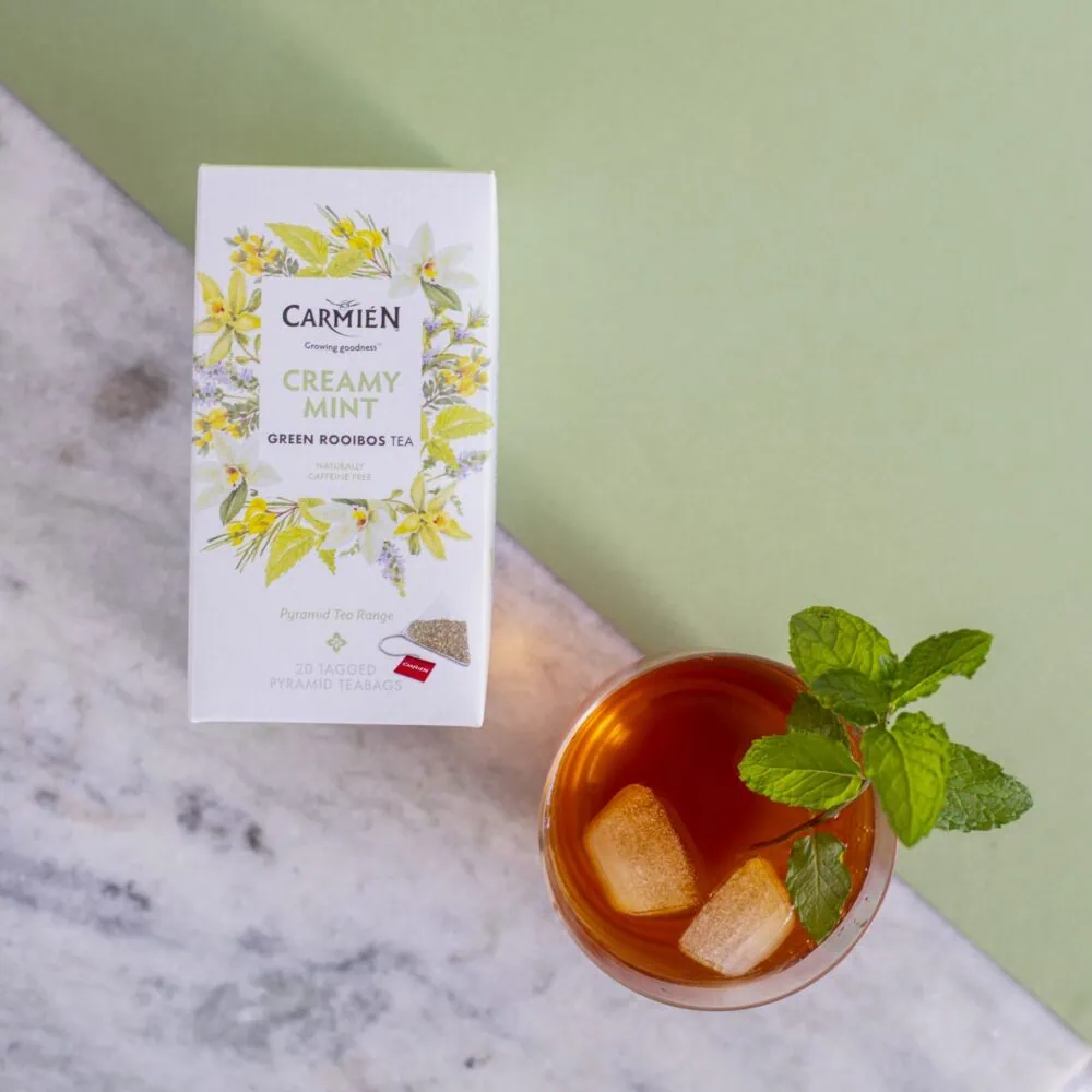 Carmién Creamy Mint Rooibos Tea box with a glass of brewed tea garnished with mint leaves, ideal for tea lovers seeking refreshing rooibos blends.