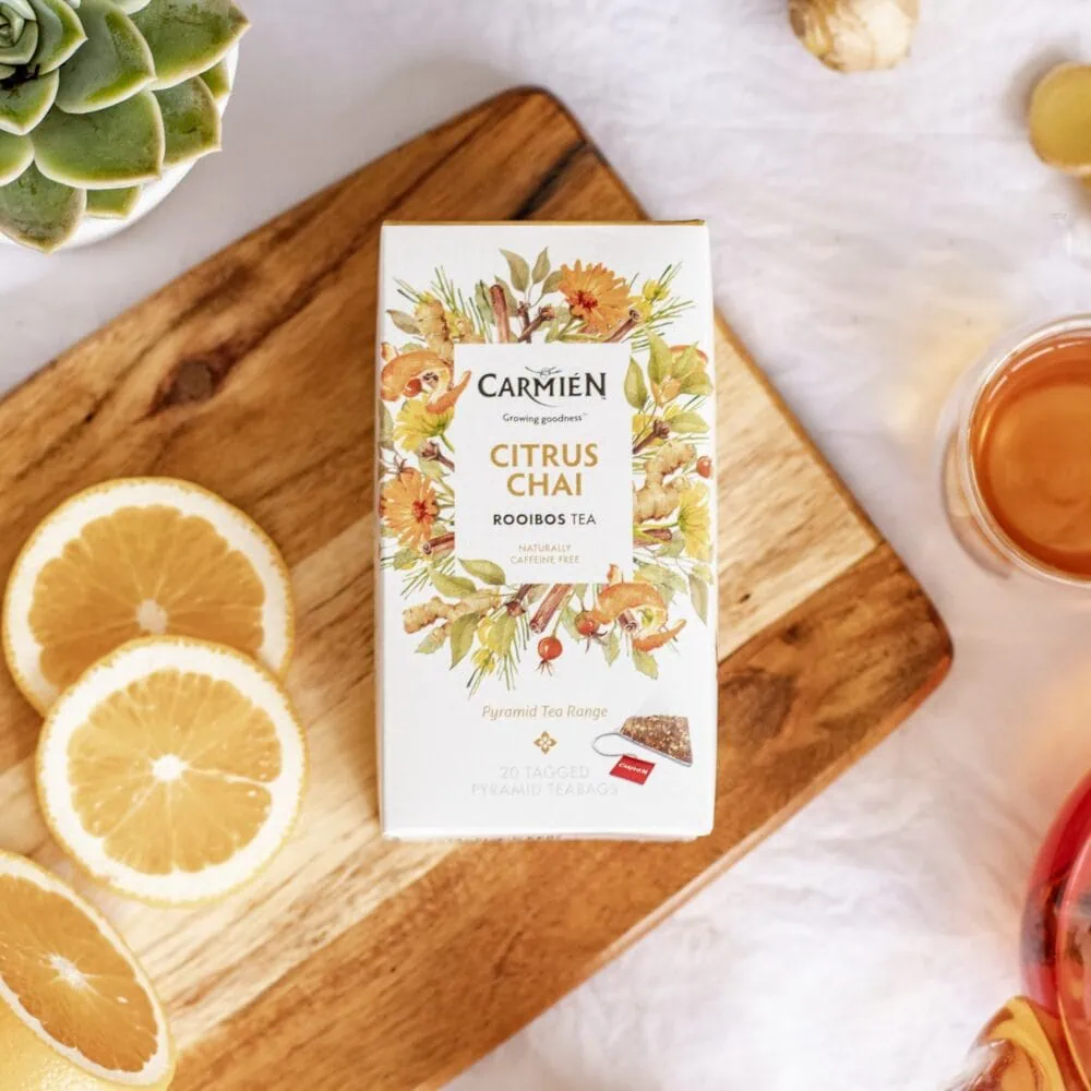 Carmién Citrus Chai Rooibos Tea box on wooden board with lemon slices and tea glass, highlighting the premium rooibos tea blend for health and flavor.