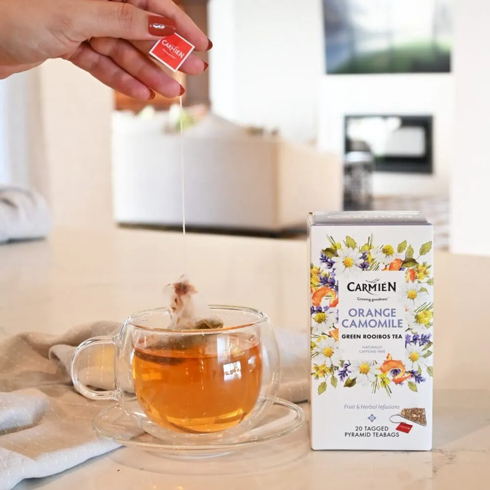 Carmién Orange Chamomile rooibos tea being prepared in a glass cup with a tea bag, showcasing the herbal infusion's vibrant color and natural ingredients.