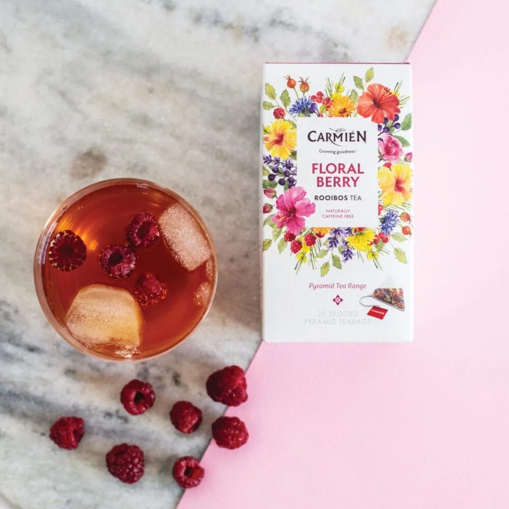 Carmién Floral Berry Rooibos Tea with fresh raspberries and pyramid teabags on a marble surface.