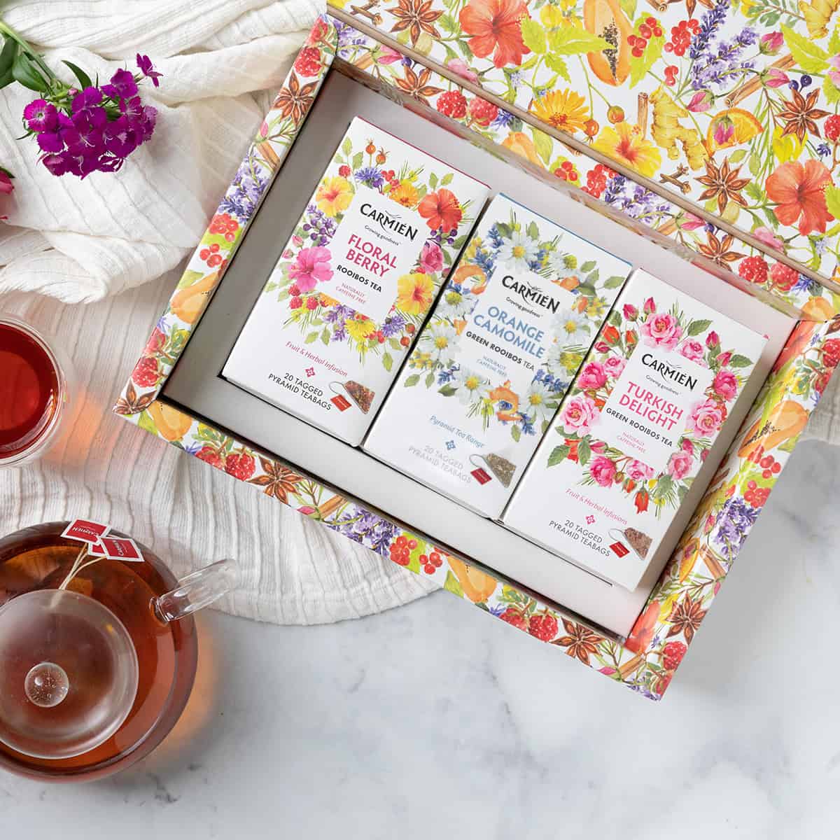 Vibrant herbal tea gift box featuring CarmiƩn Tea's floral, orange chamomile, and Turkish delight green rooibos tea varieties, beautifully packaged with botanical illustrations.