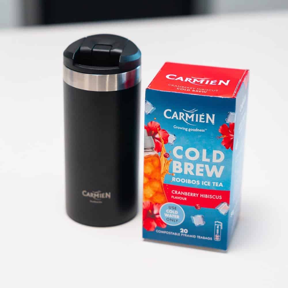 Cold brew Rooibos tea with cranberry and hibiscus flavor in a black insulated tumbler and a box of teabags. Perfect for refreshing summer drinks.