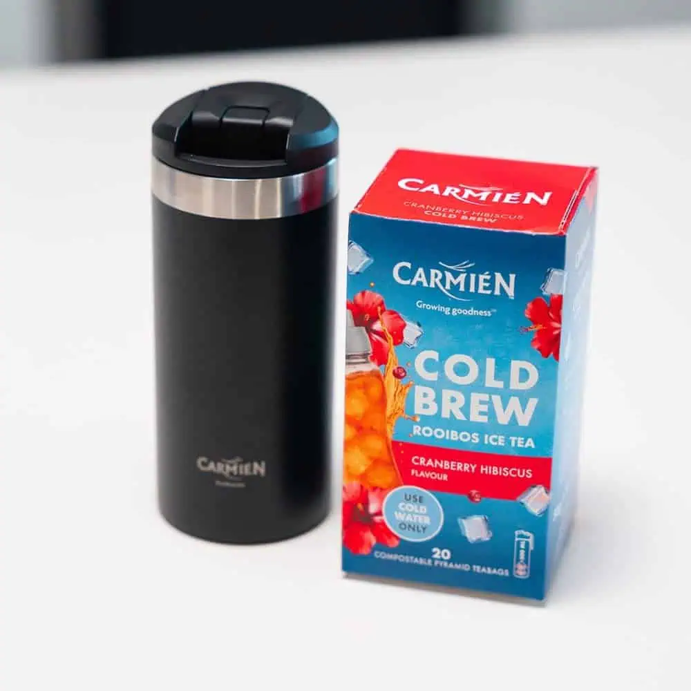 Cold brew Rooibos tea with cranberry and hibiscus flavor in a black insulated tumbler and a box of teabags. Perfect for refreshing summer drinks.