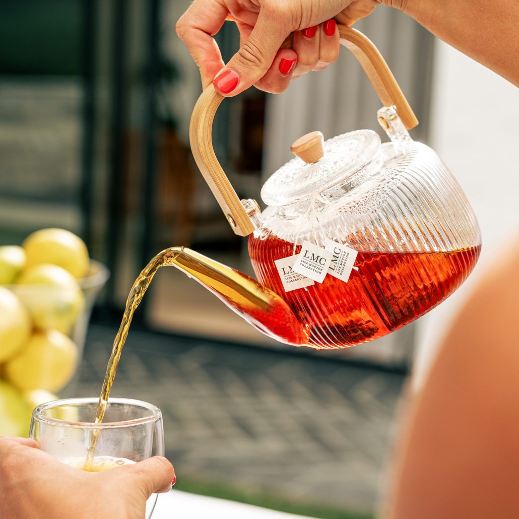 Fresh Rooibos tea being poured from a glass teapot into a clear glass, highlighting the natural, herbal tea experience.