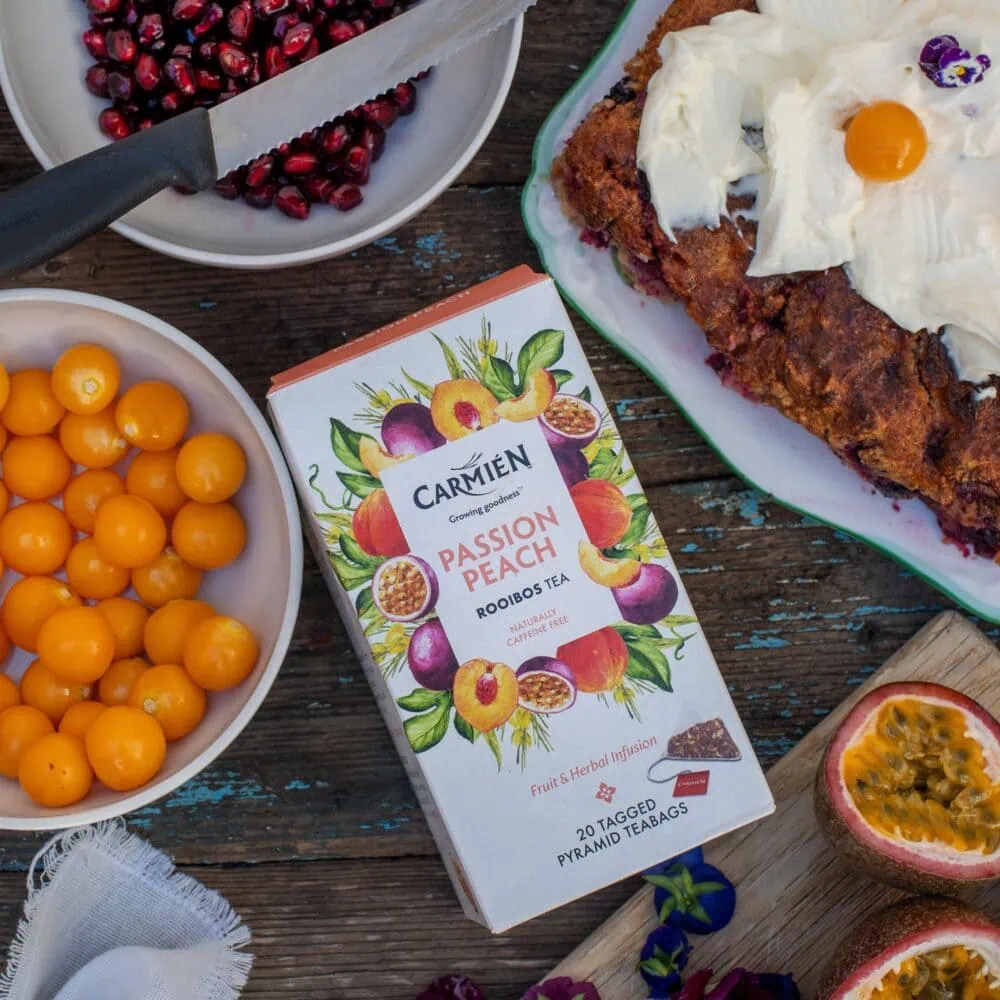 Carmién Passion Peach Rooibos Tea box with fresh fruit and baked dessert, highlighting the tea's fruity and herbal flavor profile for e-commerce sales.