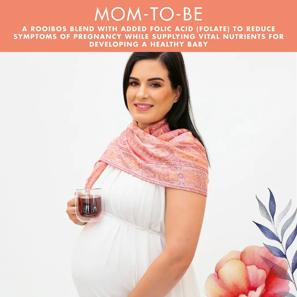 A pregnant woman smiles while holding a cup of Carmien Mom-to-Be Caffeine Free Herbal Rooibos Tea with Folic Acid