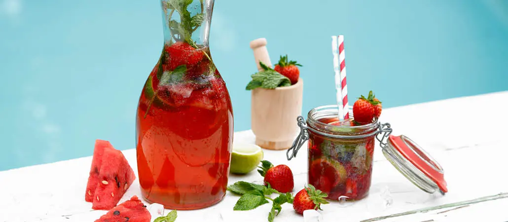 Refreshing strawberry-infused herbal tea served in a glass jar with fresh strawberries, mint, and a striped straw, perfect for a summer day.