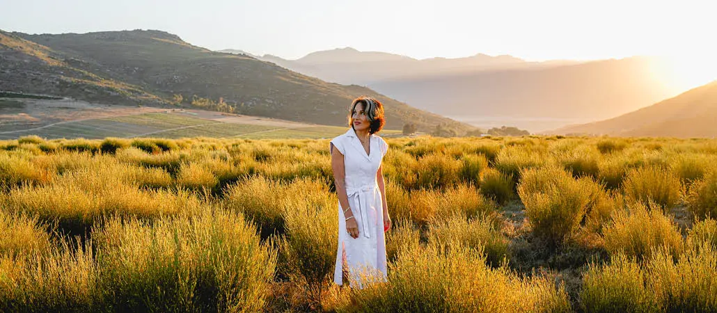 Vibrant woman standing in golden Karoo landscape during sunset, promoting Carmién Tea with natural herbal ingredients for wellness and relaxation.