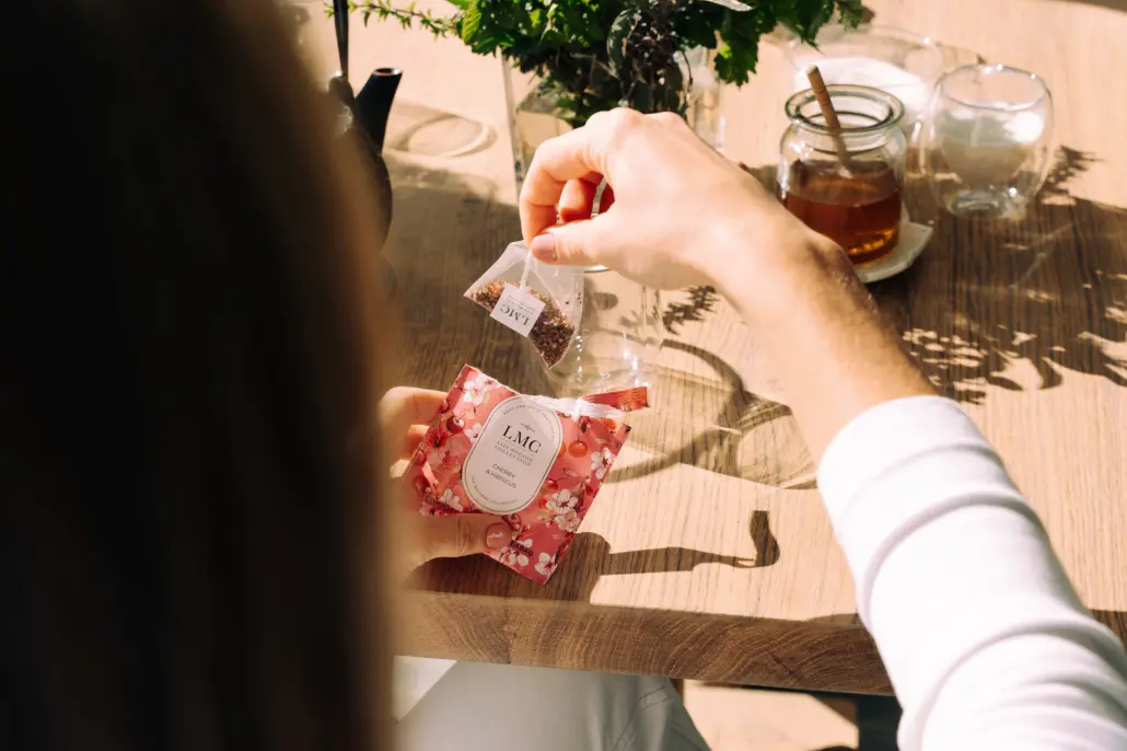 Aromatic Carmién Tea being prepared with a tea bag on a wooden table, showcasing organic herbal tea leaves, perfect for wellness and relaxation.