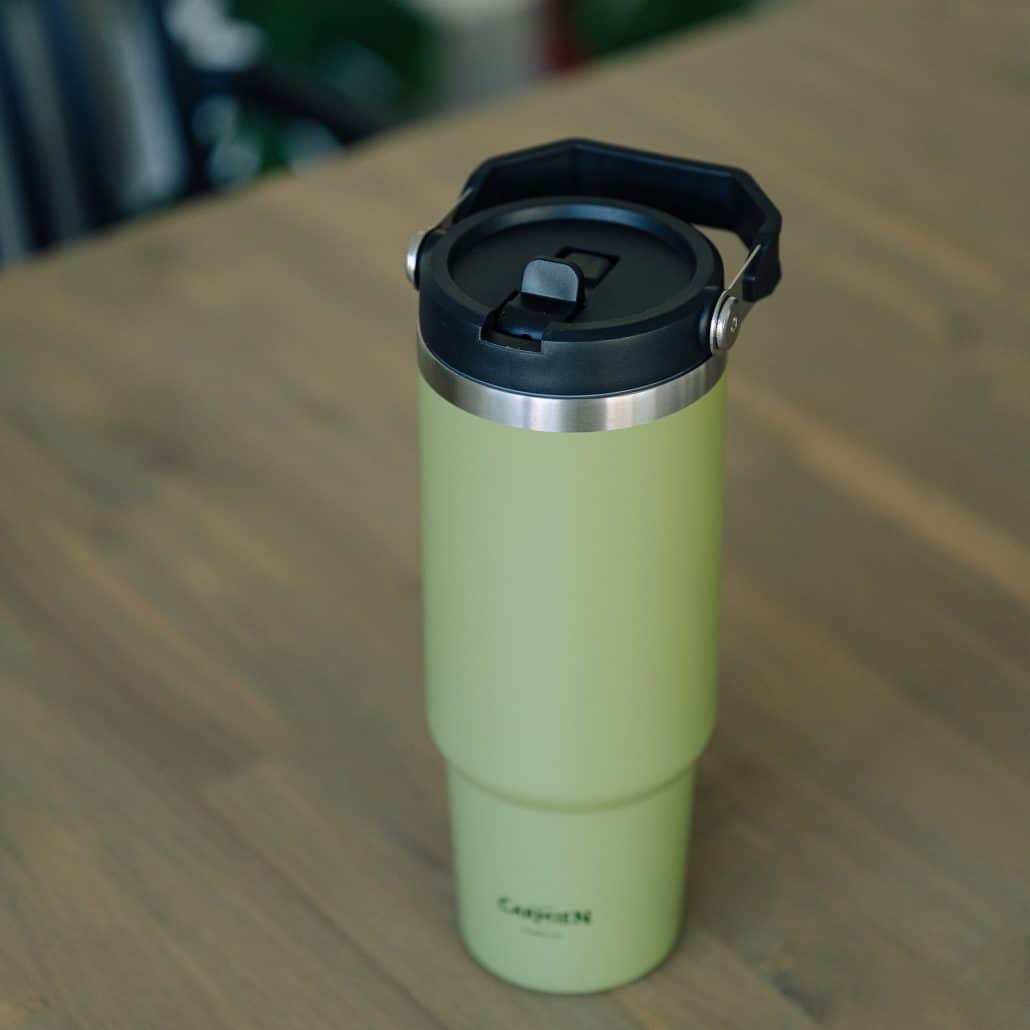 Reusable green travel coffee mug with black lid on wooden surface, ideal for enjoying Carmién Tea on the go. Perfect for tea lovers who appreciate eco-friendly beverage containers.