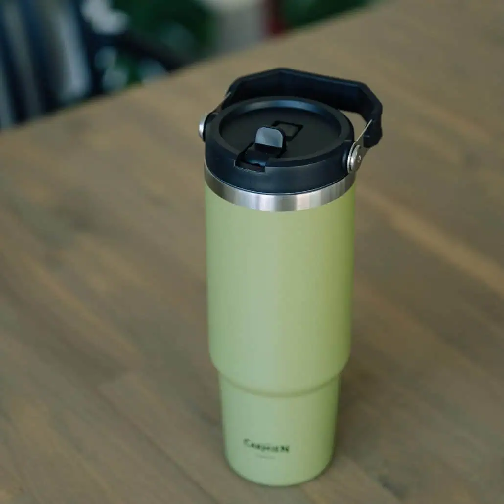 Reusable green travel coffee mug with black lid on wooden surface, ideal for enjoying Carmién Tea on the go. Perfect for tea lovers who appreciate eco-friendly beverage containers.