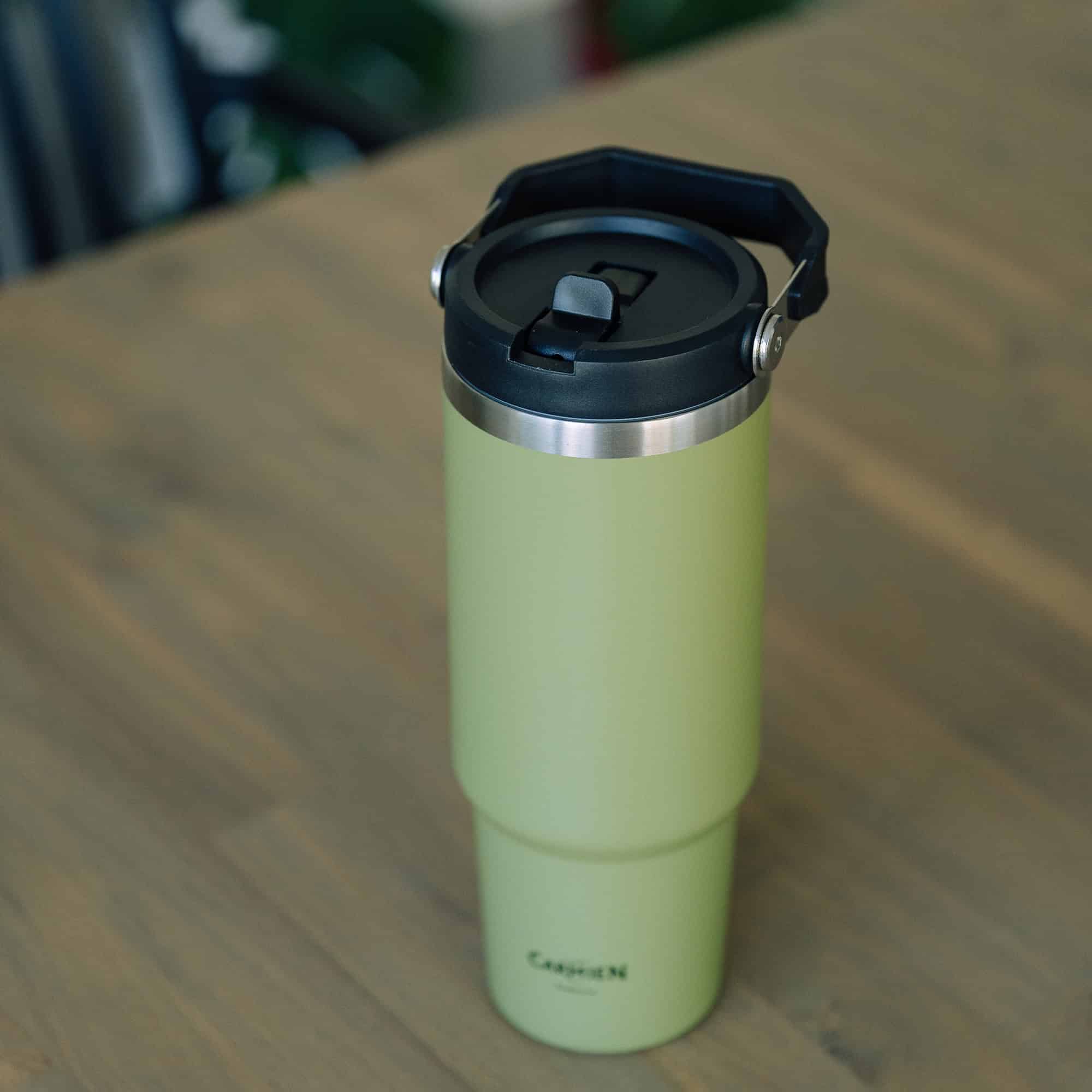 Reusable green travel coffee mug with black lid on wooden surface, ideal for enjoying Carmién Tea on the go. Perfect for tea lovers who appreciate eco-friendly beverage containers.