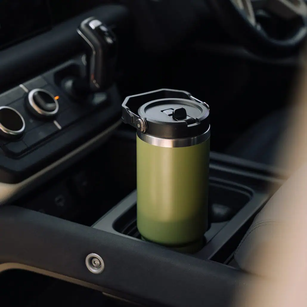A green insulated coffee tumbler in a car’s central console.