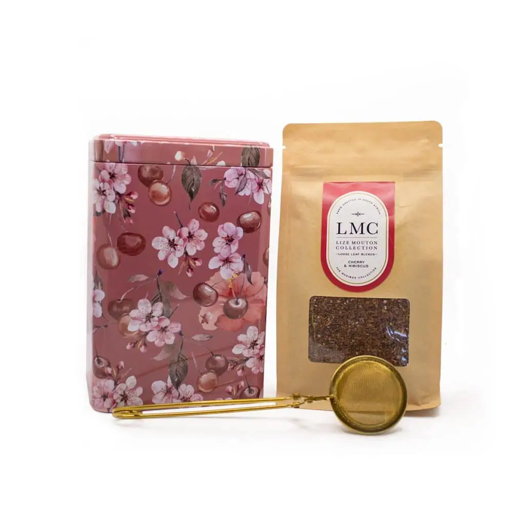 Cherry blossom-patterned tea tin with loose tea leaves package and gold tea infuser, highlighting Carmién Tea's premium South African herbal tea products.