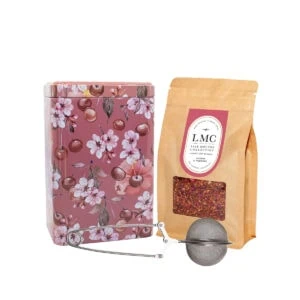 Bright pink floral tea tin with cherry blossom design, containing Carmién Tea herbal blend, accompanied by a tea infuser and a bag of dried herbal tea leaves, perfect for a relaxing South African herb.