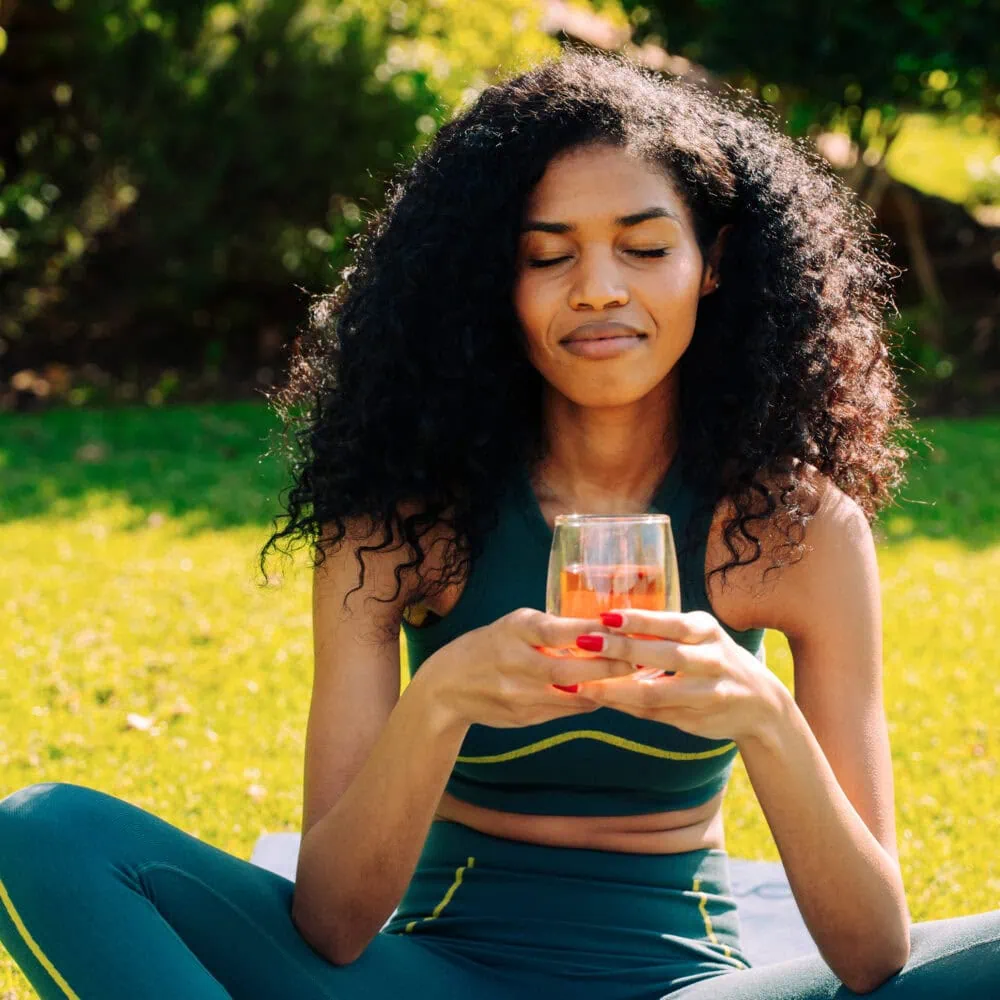 Woman enjoying a glass of Carmién herbal tea outdoors, highlighting the natural and refreshing qualities of Carmién Tea products.