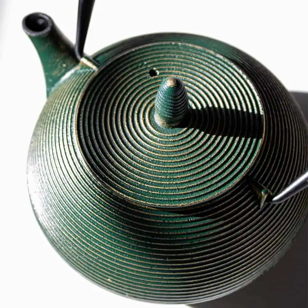 Elegant emerald green cast iron teapot with a textured spiral design, perfect for brewing and serving tea.