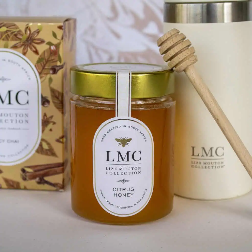 Rich, golden Citrus Honey in a glass jar with a gold lid, featuring a wooden honey dipper. Perfect for natural, South African high-quality honey and wellness products at Carmién Tea.