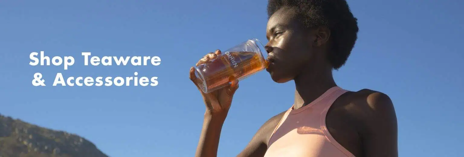Refreshing carmien tea in clear glass cup, woman drinking herbal tea outdoors under blue sky, healthy lifestyle, natural ingredients, South African wellness product, eco-friendly tea accessories.