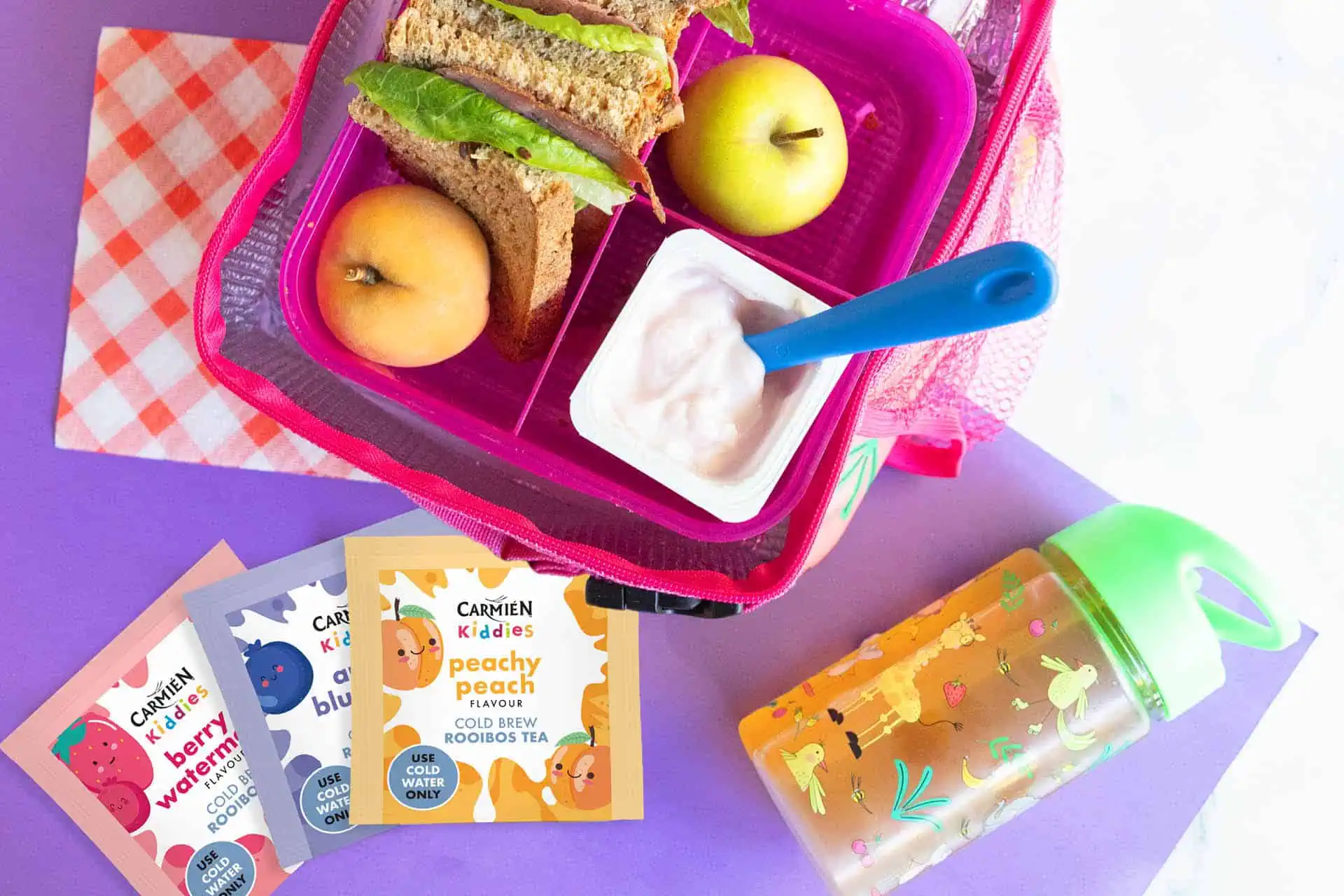 Carmién Tea lunchbox featuring fresh peach slices, a sandwich, and a container of yogurt, perfect for a healthy snack. Emphasizes natural ingredients and wellness aligned with your 2026 reset.