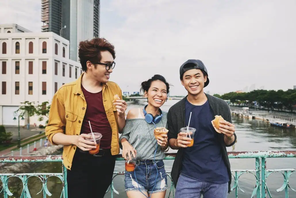 Group of young friends enjoying iced rooibos drinks outdoors near a river, promoting alcohol-free, low-calorie beverages for a healthy lifestyle.