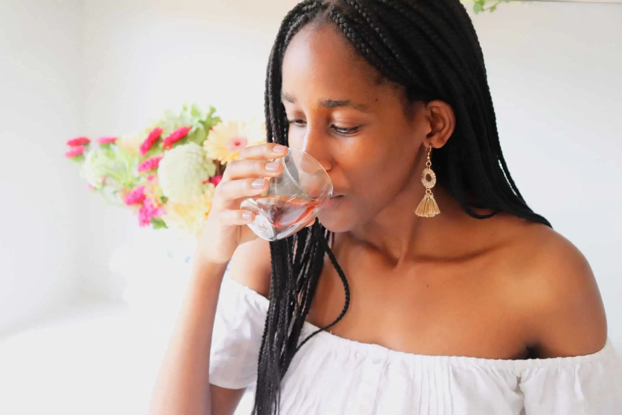 Woman enjoying a glass of Rooibos tea, promoting healthy skin from within, with a background of fresh flowers, highlighting Carmién Tea's natural skincare benefits.