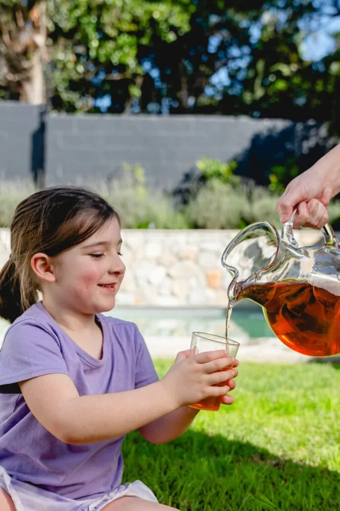 Young girl enjoying a glass of herbal tea outdoors, highlighting Carmién Tea's natural and health benefits for children.