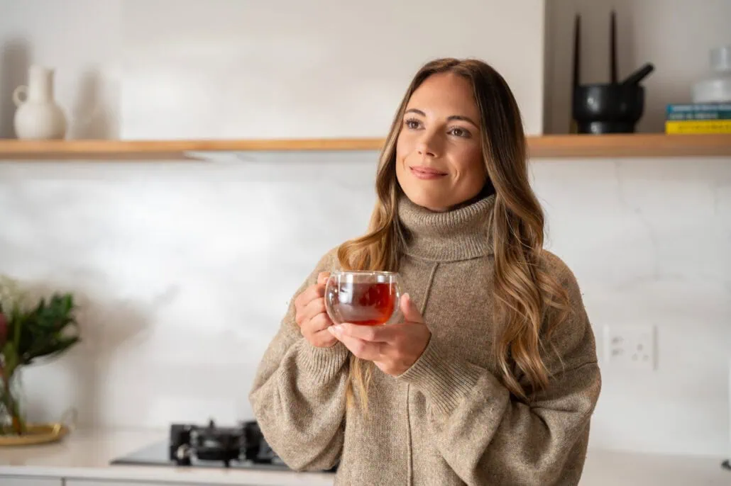 Woman enjoying a warm cup of Carmién Rooibos Tea, highlighting its soothing qualities perfect for winter relaxation.