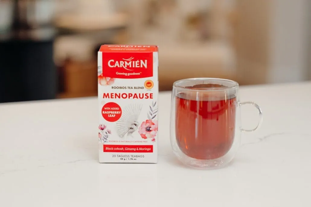 Carmién Rooibos Menopause tea with raspberry flavor in a clear glass mug on a white surface.